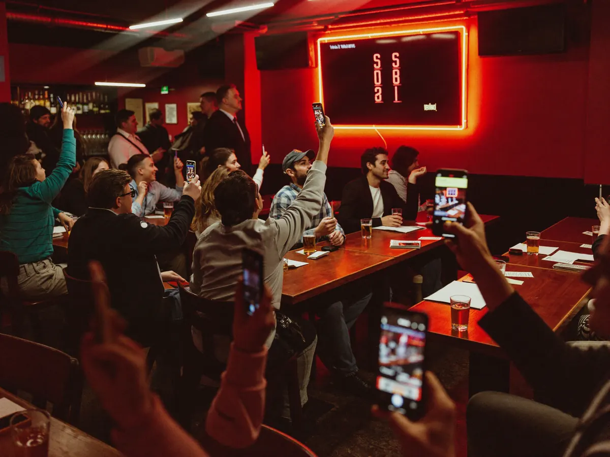 Serata quiz in un pub: i clienti alzano i telefoni verso lo schermo con i punteggi